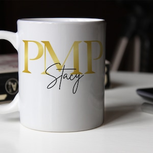 May include: White ceramic mug with a gold "PMP" and black cursive "Stacy" text.