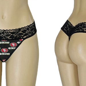 May include: Black thong underwear with a black lace trim and a repeating pattern of the San Francisco 49ers logo on a black background. The underwear is displayed on a mannequin.