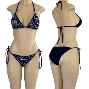 May include: A navy blue bikini with a white and silver print of the Dallas Cowboys logo and stars. The bikini top is a triangle style with adjustable straps. The bikini bottom is a tie-side style.