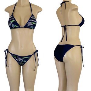 May include: A navy blue bikini with a green and white patterned top and a solid bottom. The top is a triangle style with adjustable straps and ties at the back. The bottom is a cheeky style with ties on the sides.