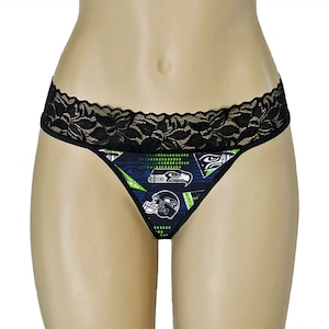 May include: Thong underwear with a black lace trim. The front panel has a navy blue pattern with green and white details, including Seattle Seahawks team logos and helmet designs. This underwear combines comfort and a sporty design.
