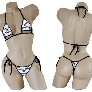 May include: A white bikini with a black trim and a Dallas Cowboys logo print. The bikini top is a halter style and the bottom is a string bikini.