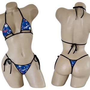 May include: A black bikini with a blue and white baseball themed print. The bikini top is a triangle style with adjustable straps and the bottom is a cheeky style with ties on the sides. The print features the Los Angeles Dodgers logo and other baseball imagery.
