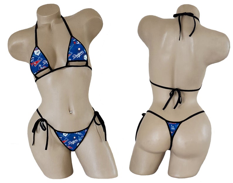 Op de afbeelding: Een zwarte bikini met een blauwe en witte baseball-print. De bikini top is een driehoekige stijl met verstelbare bandjes en de onderkant is een cheeky stijl met bandjes aan de zijkanten. De print bevat het logo van de Los Angeles Dodgers en andere baseball-afbeeldingen.