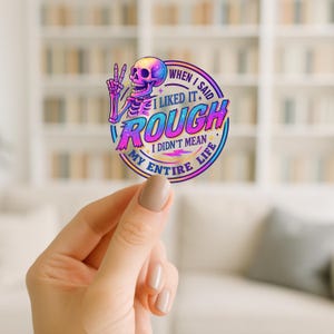 Könnte beinhalten: Ein farbenfroher Aufkleber mit einem Skelett, das ein Friedenszeichen zeigt, und Text. Der Text lautet: „Als ich sagte, ich mag es rau, meinte ich nicht mein ganzes Leben.“ Das Design verwendet leuchtende Farben.