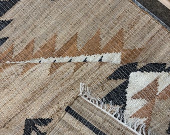 May include: A brown and black geometric patterned rug with a fringe border. The rug is made of natural fibers and has a rustic look.