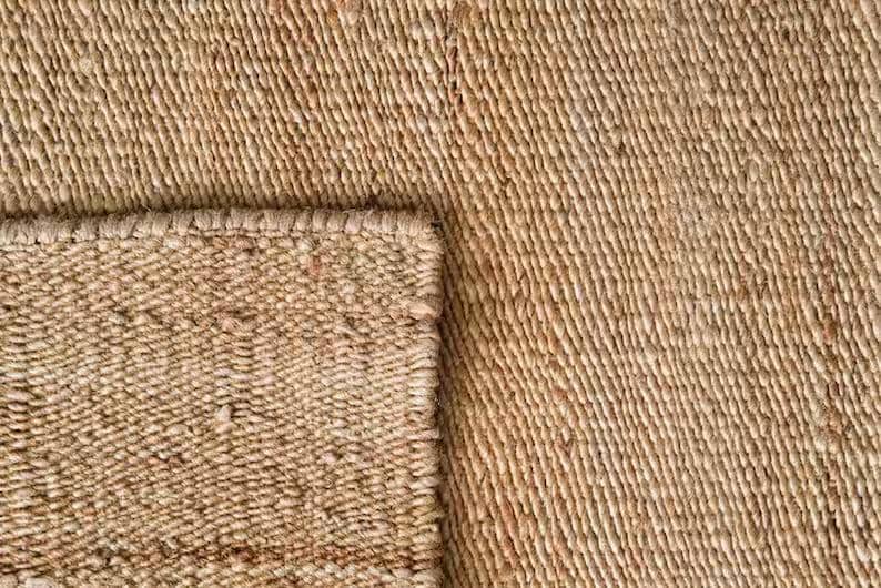 K&ouml;nnte beinhalten: Nahaufnahme eines Naturfaser-Teppichs mit gewebter Textur. Der Teppich ist hellbraun und hat eine leicht raue Oberfl&auml;che.