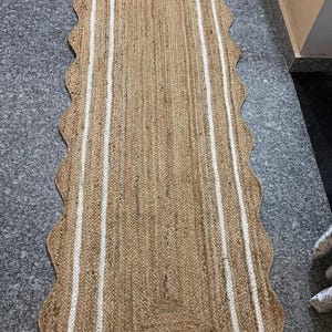 Könnte beinhalten: Ein langer, rechteckiger Jute-Teppich mit weißem Rand und gewellten Kanten. Der Teppich hat einen natürlichen, erdigen Farbton.