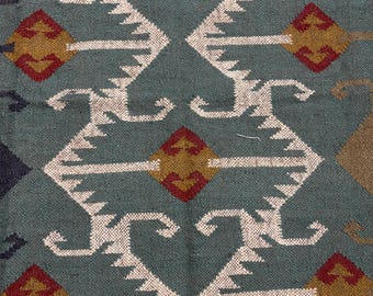 May include: A teal blue rug with a geometric pattern in white, red, and gold. The pattern features repeating diamond shapes and stylised curves.