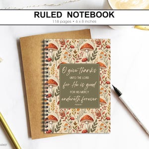 May include: Ruled notebook with a mushroom and floral design. The cover features a quote and is 15 x 20 cm with 118 pages. A gold pen and a roll of decorative tape are also in the image.