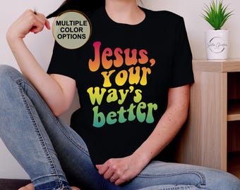 May include: Black t-shirt with the text "Jesus, your way's better" in a colorful, retro font. The shirt has multiple color options. A small potted plant sits on a wooden surface.