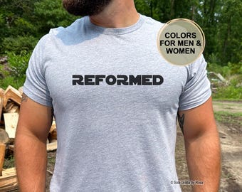 Op de afbeelding: Een lichtgrijs t-shirt met korte mouwen en het woord REFORMED in dikke zwarte hoofdletters op de borst. Een cirkelvormige beige afbeelding in de rechterbovenhoek bevat de tekst COLORS FOR MEN & WOMEN.