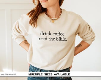May include: A cream-coloured sweatshirt featuring the text "drink coffee. read the bible." in black. This long-sleeved top is made of a soft material and is suitable for casual wear. Multiple sizes are available.