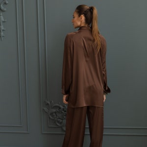 K&ouml;nnte beinhalten: Ein braunes Satin-Pyjama-Set mit einem lang&auml;rmeligen Oberteil und einer weiten Hose.
