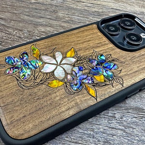 以下が含まれることがあります： 青、白、黄色のアクセントが施された花柄のウッド製携帯電話ケース。ケースには黒いバンパーとカメラの切り抜きがあります。