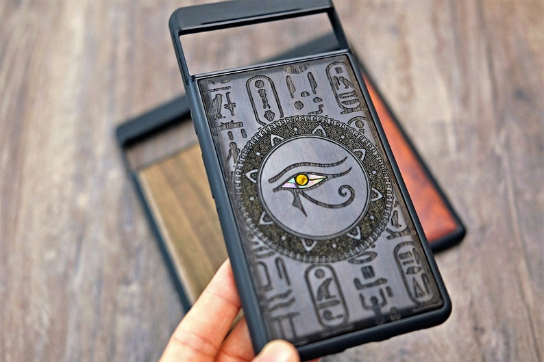 Op de afbeelding: Zwarte telefoonhoes met een transparant achterpaneel met een gegraveerd ontwerp van het oog van Horus omringd door hi&euml;rogliefen.