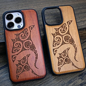 May include: Two wooden phone cases with a black trim. The cases feature a carved design of manta rays with intricate patterns. One case is a dark reddish brown wood, the other is a lighter brown wood.