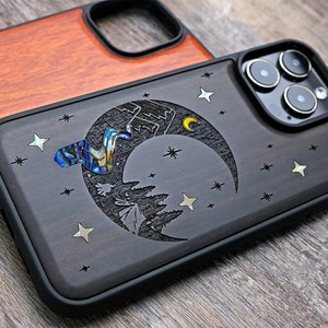 Puede incluir: Una funda de tel&eacute;fono de madera negra con un dise&ntilde;o de luna creciente y estrellas. La luna est&aacute; incrustada con n&aacute;car de abul&oacute;n iridiscente. La funda tiene un parachoques de goma negro.