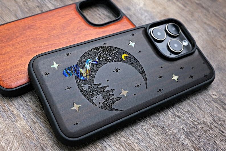 Puede incluir: Una funda de tel&eacute;fono de madera negra con un dise&ntilde;o de luna creciente y estrellas. La luna est&aacute; incrustada con n&aacute;car de abul&oacute;n iridiscente. La funda tiene un parachoques de goma negro.