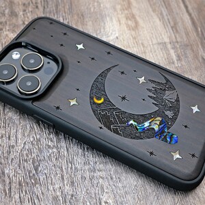 Puede incluir: Una funda para tel&eacute;fono de madera negra con un dise&ntilde;o de luna creciente y estrellas. La luna est&aacute; hecha de n&aacute;car y tiene una peque&ntilde;a luna creciente en su interior. La funda tiene un parachoques de goma negro.