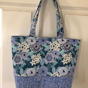May include: A blue and white floral tote bag with a blue and white swirl pattern on the bottom. The bag has two long handles.