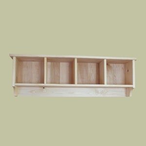 May include: A natural wood wall shelf with four open cubbies. The shelf has a simple design and is perfect for storing small items.