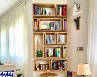 May include: A wooden bookshelf with multiple shelves filled with books. The shelves are arranged in a grid pattern and are attached to a white wall. A small table with a round top sits in front of the bookshelf.