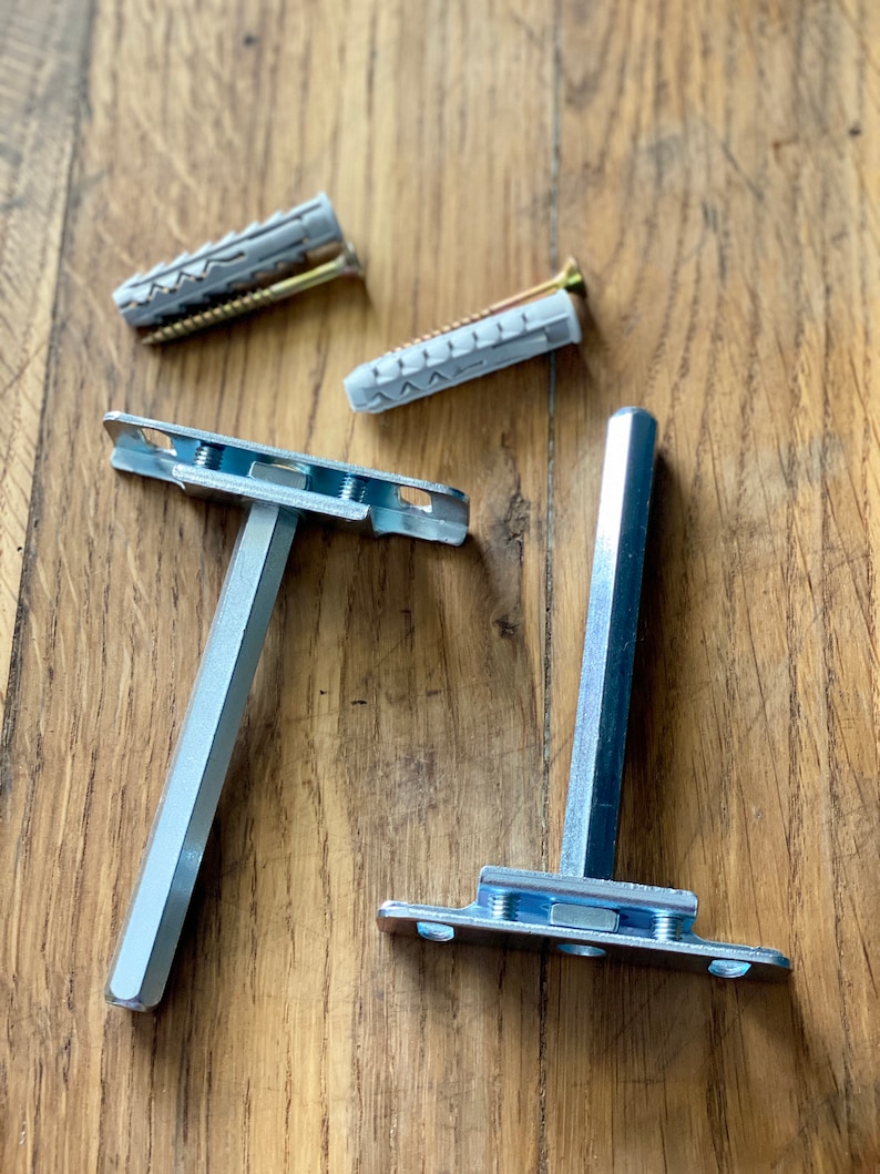 May include: Two silver metal shelf brackets with mounting screws and plastic anchors. The brackets are on a wooden surface.