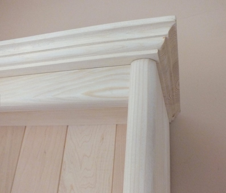 May include: A light-colored wooden shelf unit featuring a vertical cylindrical support pillar on the right side and a horizontal crown molding top piece with decorative grooves, showcasing the natural grain of the unfinished wood.