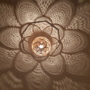 May include: A close-up of a decorative light fixture casting a patterned shadow on a ceiling. The light fixture is made of metal and has a geometric design. The shadow is a repeating pattern of circles and lines.