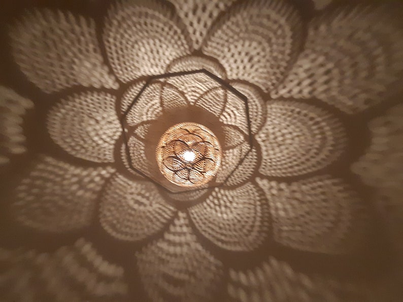 May include: A close-up of a decorative light fixture casting a patterned shadow on a ceiling. The light fixture is made of metal and has a geometric design. The shadow is a repeating pattern of circles and lines.