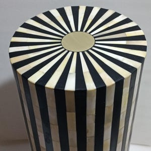 May include: A black and white striped cylindrical stool with a gold top. The stool is made of inlaid bone and wood.