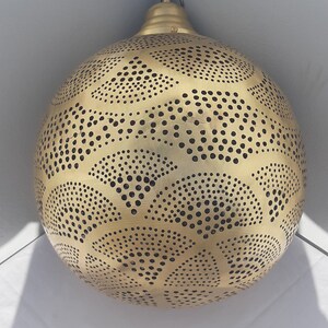 May include: A gold-colored, round, metal pendant light fixture with a decorative, intricate pattern of small circles and cut-outs.