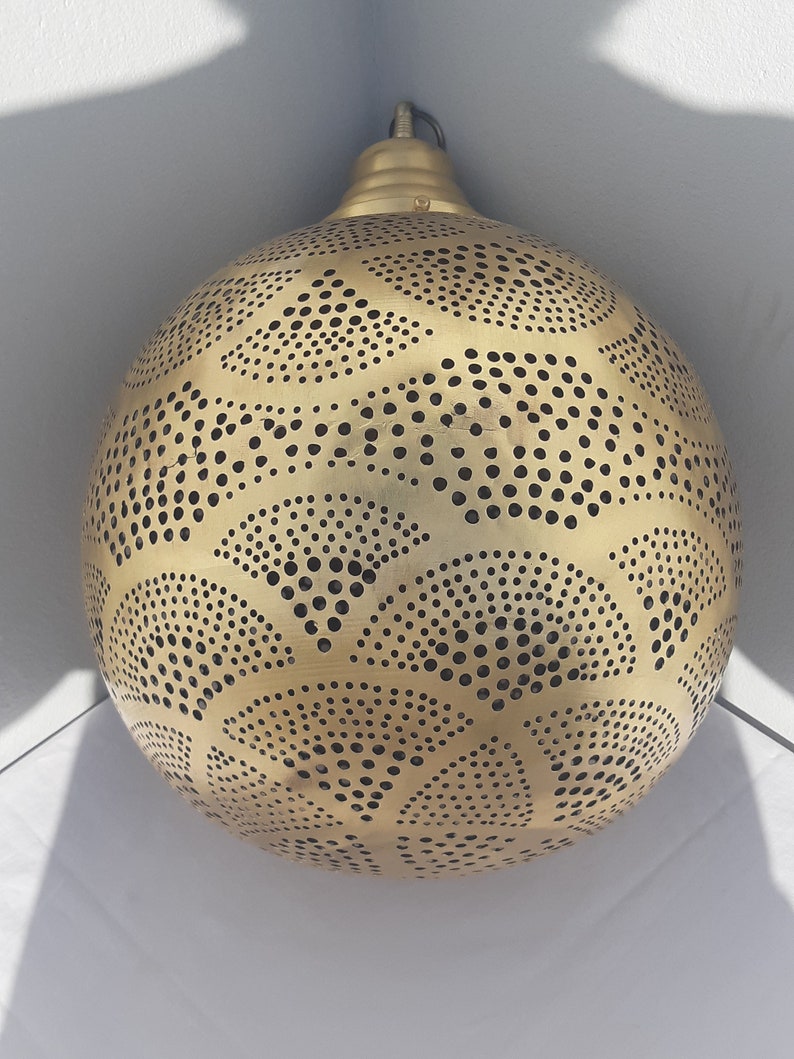 May include: A gold-colored, round, metal pendant light fixture with a decorative, intricate pattern of small circles and cut-outs.