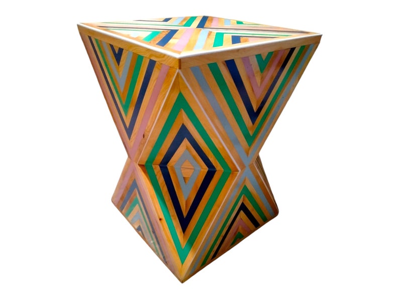 K&ouml;nnte beinhalten: Ein geometrischer Holzhocker mit einem farbenfrohen Streifenmuster. Der Hocker ist aus Holz und in den Farben Gr&uuml;n, Blau, Rosa und Gelb gestrichen.
