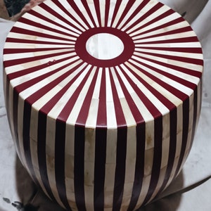 May include: A round, white and burgundy striped stool with a white circle in the centre of the top. The stool is made of bone and has a polished finish.