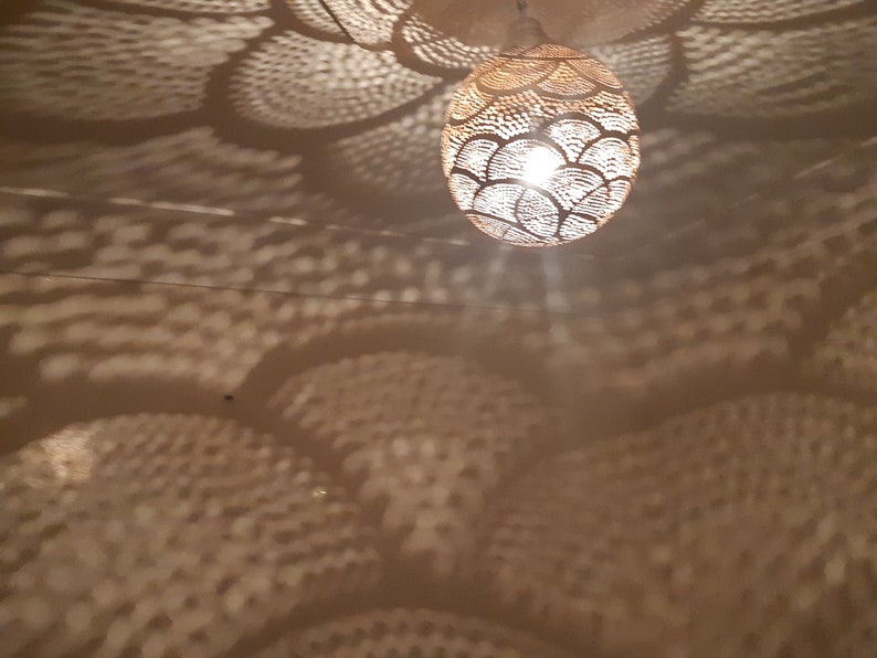 May include: A white ceiling with a round, woven, light fixture hanging from it. The light fixture casts a pattern of overlapping circles on the ceiling.
