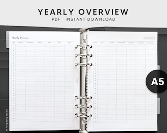 May include: A white A5 size yearly planner with a black binder. The planner has a tab for each month of the year and a column for dates. The text "Yearly Overview" is at the top of the page.