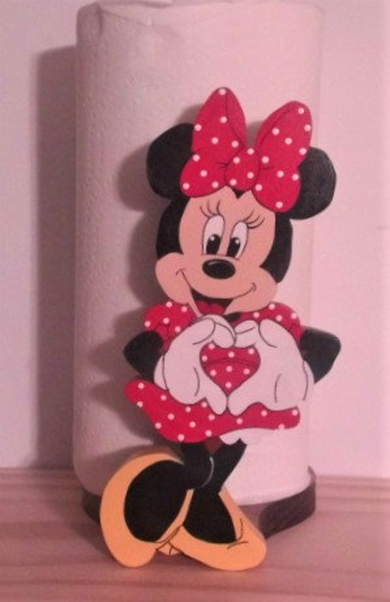 May include: A red and white Minnie Mouse paper towel holder. Minnie is wearing a red dress with white polka dots and is making a heart shape with her hands.