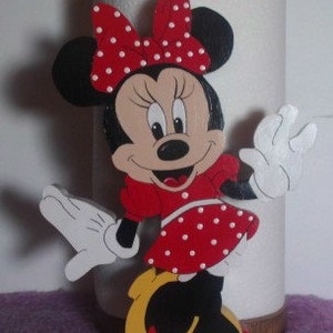 Puede incluir: Un recorte de madera de Minnie Mouse, pintado en rojo, blanco y negro. Lleva un vestido rojo con lunares blancos y un lazo negro con lunares blancos. Tiene una gran sonrisa y est&aacute; saludando.