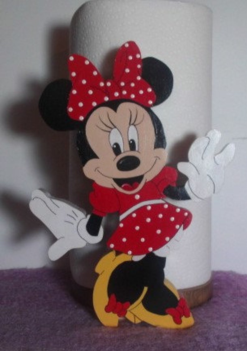 Puede incluir: Un recorte de madera de Minnie Mouse, pintado en rojo, blanco y negro. Lleva un vestido rojo con lunares blancos y un lazo negro con lunares blancos. Tiene una gran sonrisa y est&aacute; saludando.