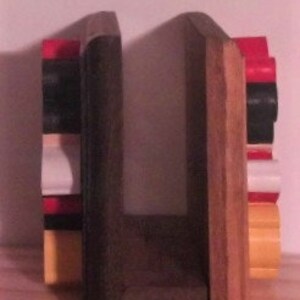 May include: A pair of wooden bookends with a rustic finish. The bookends are painted in shades of red, black, and yellow. The bookends are designed to hold books upright.