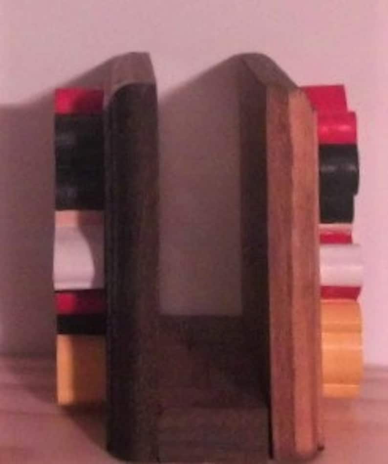 May include: A pair of wooden bookends with a rustic finish. The bookends are painted in shades of red, black, and yellow. The bookends are designed to hold books upright.