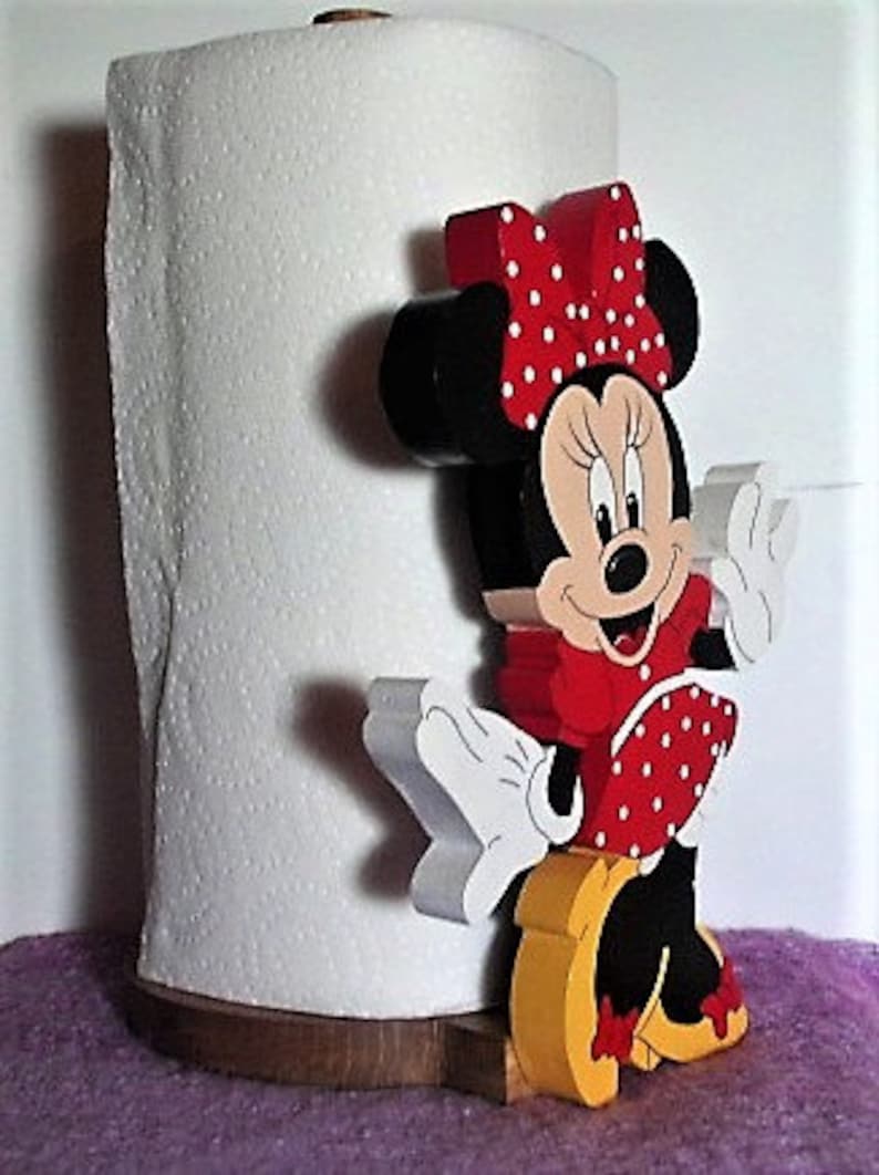 Puede incluir: Un soporte de papel de cocina de madera con una imagen de dibujos animados de Minnie Mouse. Minnie lleva un vestido rojo con lunares blancos y un lazo rojo con lunares blancos. Lleva zapatos negros y tiene una cara blanca y negra.