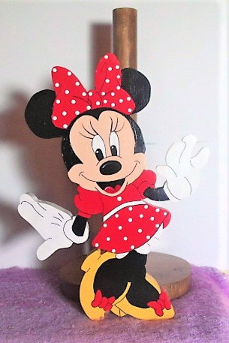 Puede incluir: Un recorte de madera de Minnie Mouse, pintado en rojo, negro y blanco. Lleva un vestido rojo con lunares blancos y un lazo rojo con lunares blancos. Est&aacute; sonriendo y saludando.