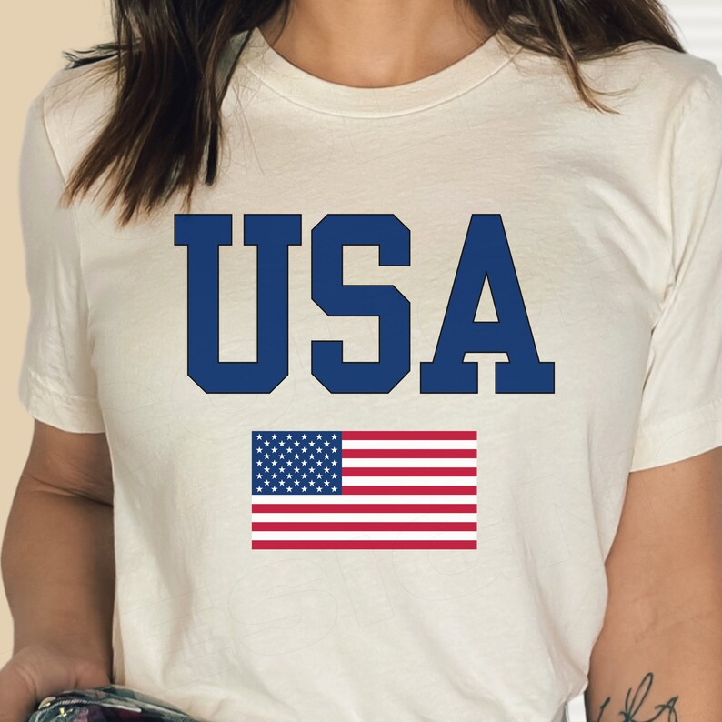 May include: White t-shirt with the word "USA" printed in blue letters and an American flag below it.