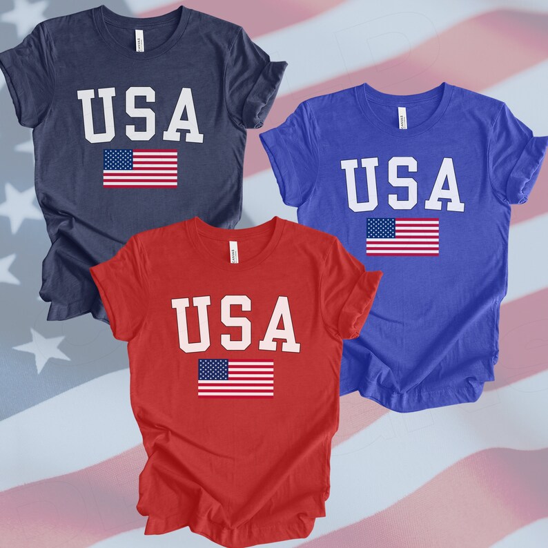 May include: Three t-shirts with the word "USA" printed in white letters and a small American flag printed below. The shirts are navy blue, royal blue, and red.