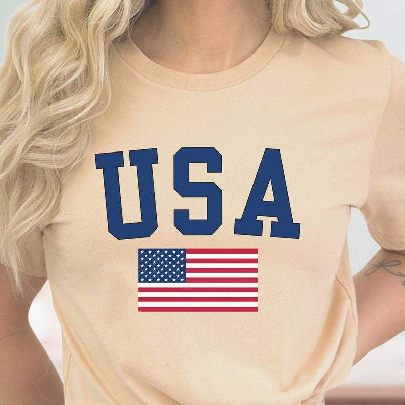 May include: A beige t-shirt with the word "USA" printed in blue letters and an American flag graphic below.