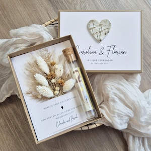 Könnte beinhalten: Ein Hochzeitsgeschenk-Set mit zwei Boxen. Eine Box enthält eine Karte mit Trockenblumen und einem Glasröhrchen mit Korken. Die andere Box hat eine Karte mit einem Herz und den Namen "Carolina & Florian" und dem Datum "05. Oktober 2024".