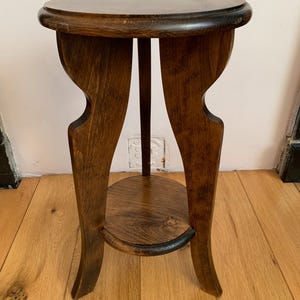 Può includere: Un tavolino da salotto in legno marrone scuro con piano rotondo e un ripiano inferiore. Il tavolino ha un design unico con gambe curve.